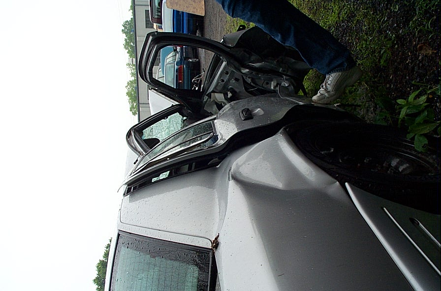 Damaged silver sedan with doors open, showing interior damage. Another blue vehicle is visible behind it