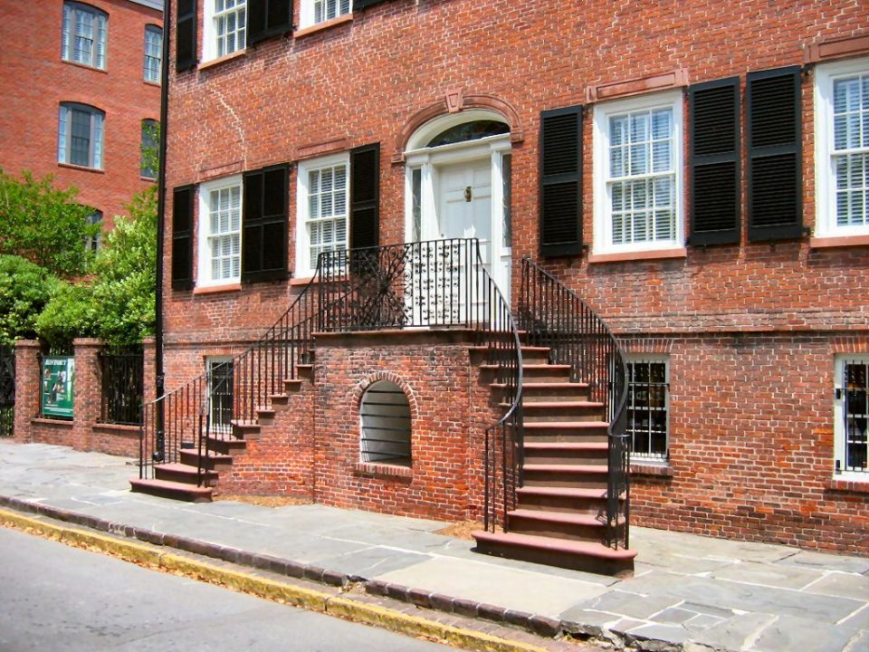 Brick building with a curved staircase leading to a white door and black shutters