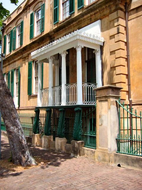 1985 Ford LTD Crown Victoria - A historic building features a prominent white balcony with decorative railings and columns, set against a tan facade and green shutters.