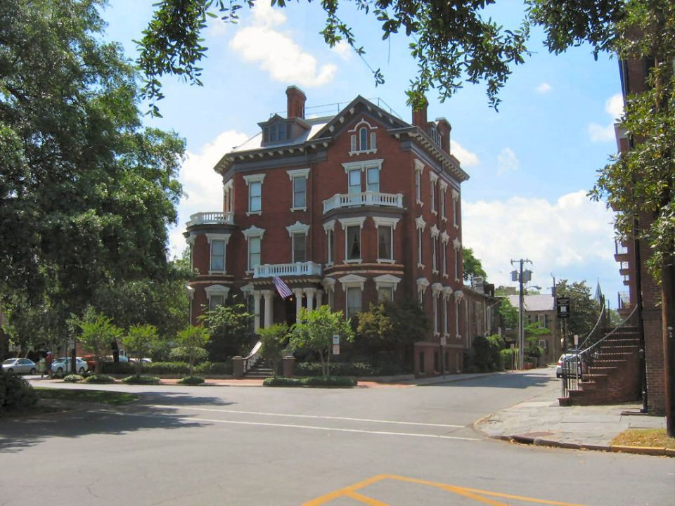Historic brick building on a street corner with trees and a blue sky
