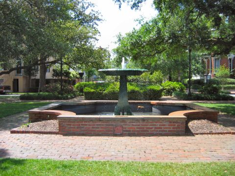 1985 Ford LTD Crown Victoria - A decorative fountain sits in a park setting with lush greenery and trees surrounding it.