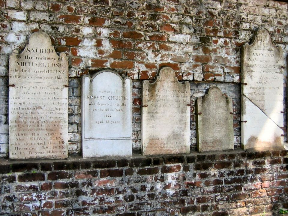 Old gravestones embedded in a weathered brick wall in a cemetery