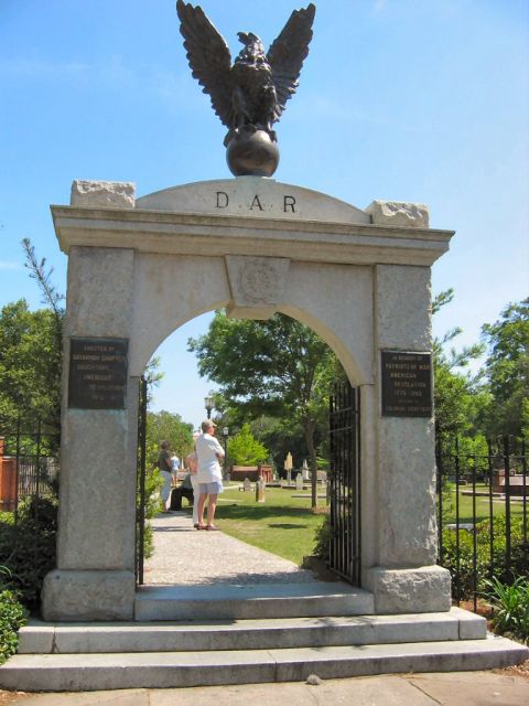 1985 Ford LTD Crown Victoria - Monumental archway with eagle sculpture and plaques, marking entrance to a historic cemetery.
