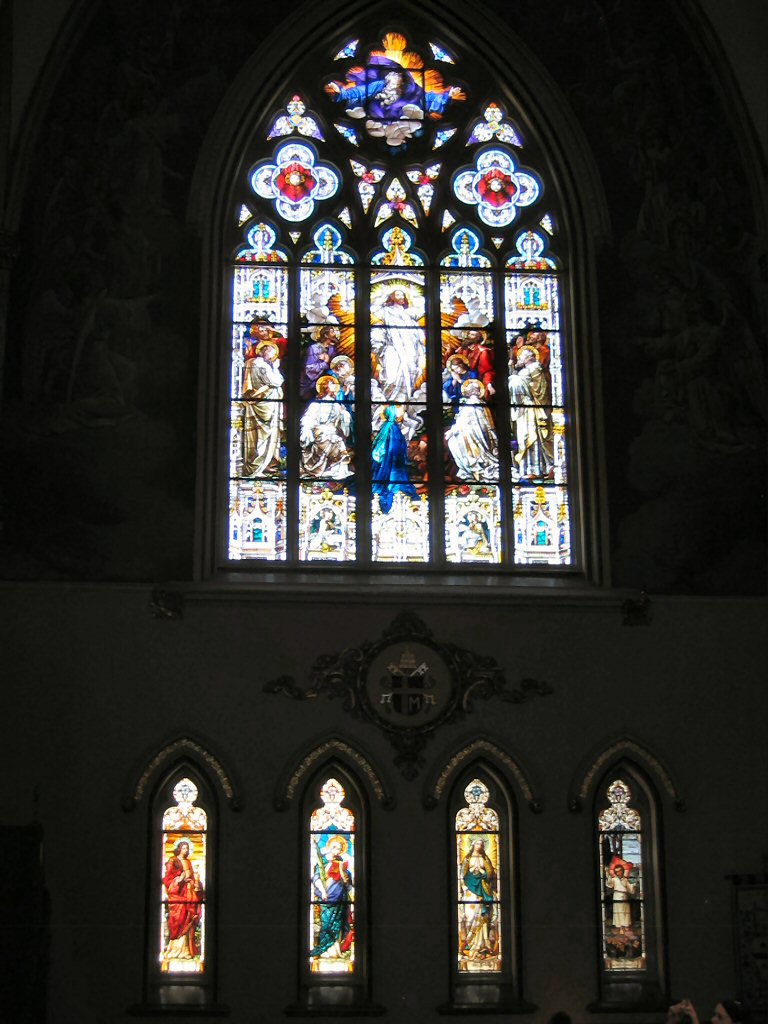 Large gothic stained glass window depicting Jesus and disciples above smaller stained glass windows with figures
