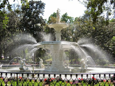1985 Ford LTD Crown Victoria - A large, ornate fountain sprays water in a park surrounded by trees and a decorative fence.