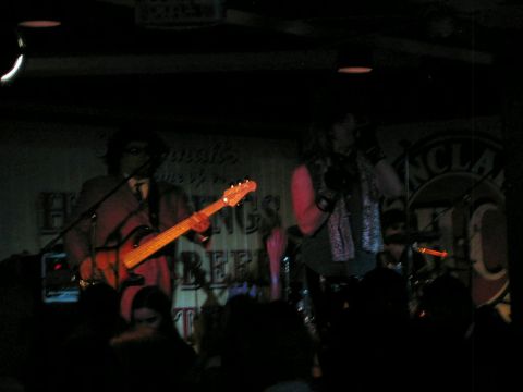 1985 Ford LTD Crown Victoria - A band performs live on stage at a venue with a crowd watching.