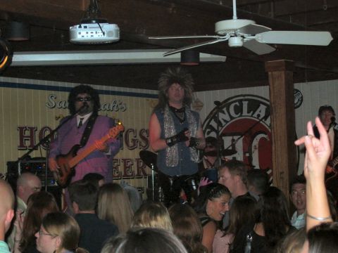 1985 Ford LTD Crown Victoria - A band performs on stage in front of a decorated wall, with an audience watching.