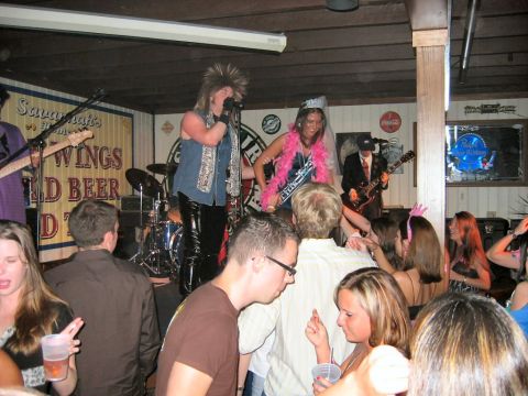 1985 Ford LTD Crown Victoria - A lively scene unfolds at a bar as a band plays on stage and patrons enjoy the atmosphere.