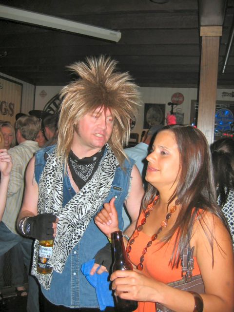 1985 Ford LTD Crown Victoria - Two people converse at a bar, one wearing a distinctive wig and outfit.