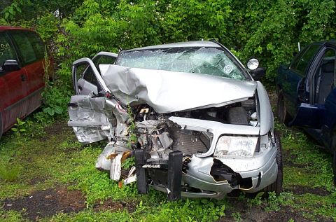 2001 Ford Crown Victoria - Front-collision-damaged silver sedan with smashed hood, fender and windshield parked among other cars in a salvage lot.