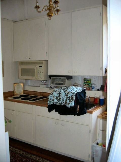 1985 Ford LTD Crown Victoria - A cluttered kitchen scene with appliances and cabinets. Clothes are draped over the counter near the sink.