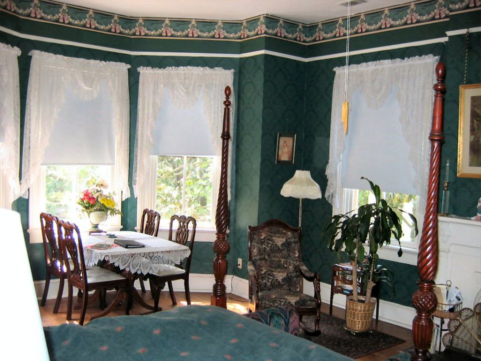 Interior of a room with a dining table, chairs, a patterned armchair, and a four-poster bed
