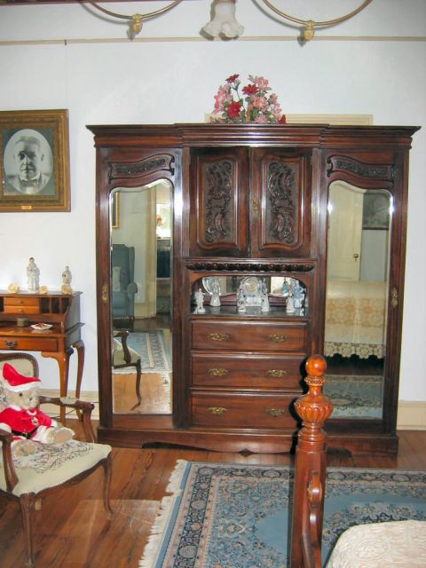 1985 Ford LTD Crown Victoria - A vintage armoire dominates the room, reflecting a bed and a doorway, with a teddy bear seated nearby.