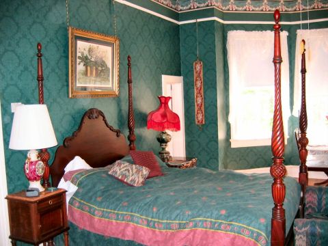 1985 Ford LTD Crown Victoria - This bedroom features a large four-poster bed with a green and pink comforter, set against a backdrop of green damask wallpaper.
