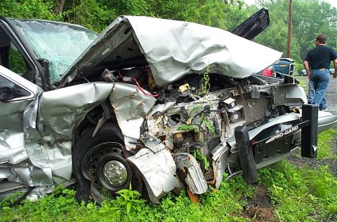 2001 Ford Crown Victoria - A heavily damaged 2001 Ford Crown Victoria sits on the side of the road after a collision, with a man standing nearby.