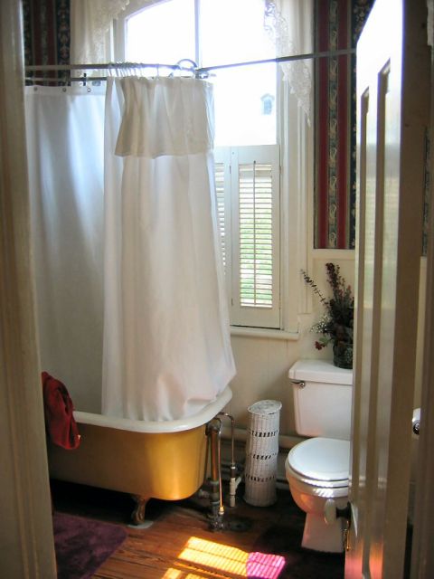 1985 Ford LTD Crown Victoria - Sunlight streams into a bathroom, illuminating a clawfoot tub and toilet.