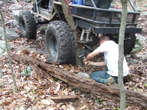 1969 Ford Bronco - Man attempts to free an off-road vehicle that is stuck against a tree on a rocky, wooded trail.
