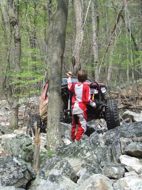 1969 Ford Bronco - A child in racing gear stands near a modified off-road vehicle on a challenging rocky terrain.