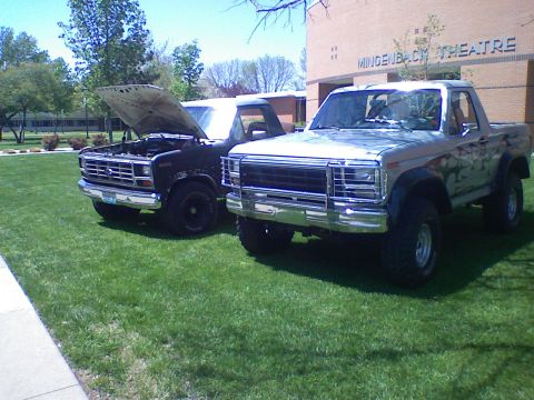 1985 Ford Bronco - Two Ford Broncos are parked on a grassy lawn in front of a brick building with "MINDENBACH THEATRE" visible.