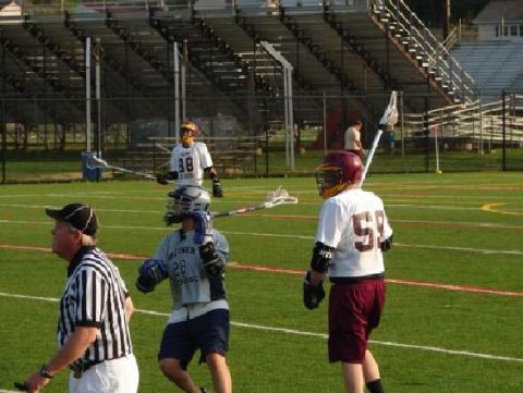 1997 Dodge 1500 - Players and a referee are on a lacrosse field with stadium seating in the background.