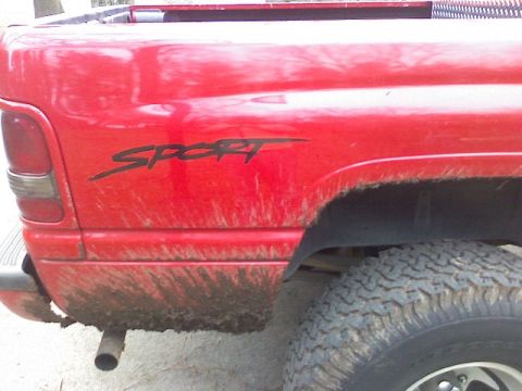 1997 Dodge 1500 - Rear view of a red pickup truck showing a "SPORT" decal on the quarter panel, covered in mud.