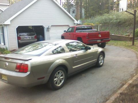 1997 Dodge 1500 - A silver Ford Mustang coupe and a red pickup truck are parked in a driveway next to a garage.