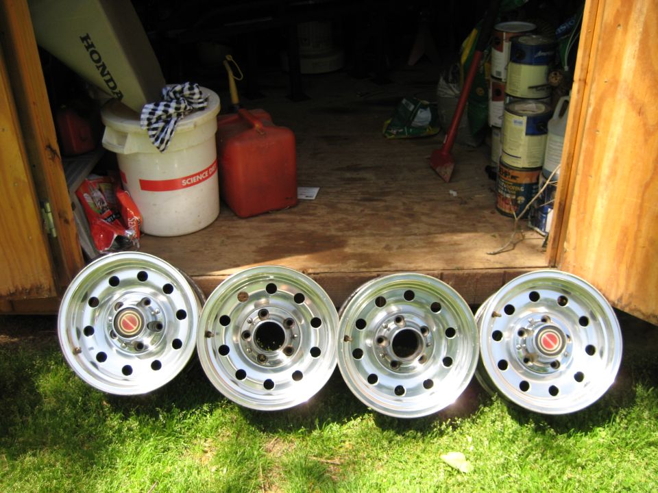 four aluminum wheels with red center caps, sitting on grass in front of a shed