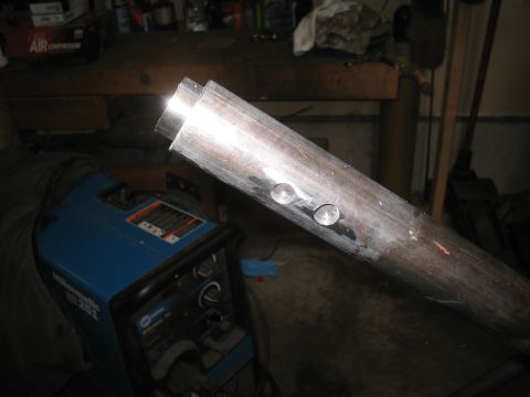 1979 Ford Bronco - Close-up of a metal pipe with two bolts, with a Miller welding machine in the background.