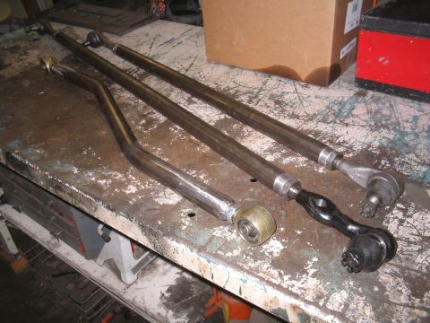 1979 Ford Bronco - Custom steering linkage components are laid out on a worn metal workbench, ready for installation.