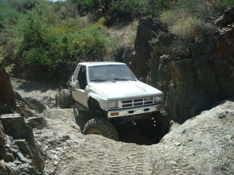 1986 Toyota Hilux - White Toyota pickup truck with large tires navigating a rocky off-road trail.
