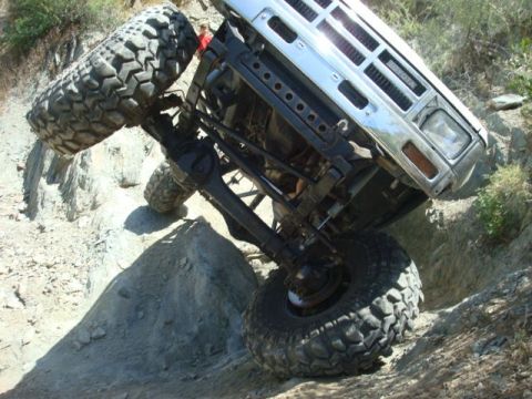 1986 Toyota Hilux - This modified truck is navigating a steep, rocky terrain, with its wheels angled precariously.