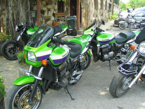 1981 Kawasaki Bayou - Multiple green and white Kawasaki motorcycles are parked outside a stone building.
