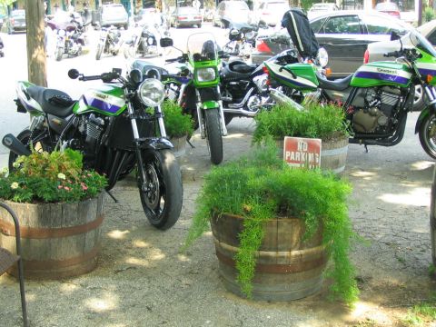 1981 Kawasaki Bayou - Multiple Kawasaki motorcycles are parked outside, with decorative planters and other vehicles nearby.