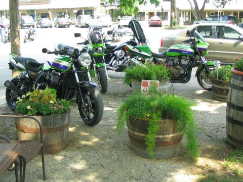 1981 Kawasaki Bayou - Several motorcycles are parked in front of a building, with planters in the foreground.