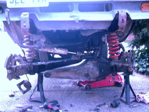 1987 Ford Bronco II - The rear suspension of a vehicle is shown on jack stands, with red springs and repair tools nearby.