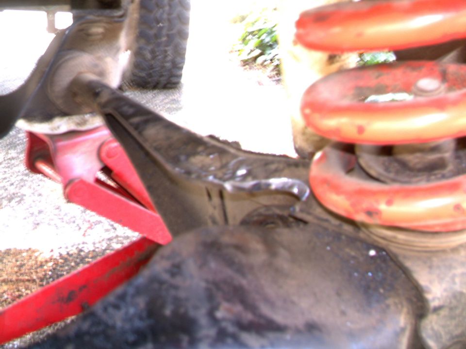 Underside of Bronco II front suspension with red coil spring, differential, and red floor jack