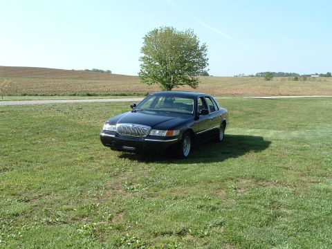 2001 Mercury Grand Marquis - A black 2001 Mercury Grand Marquis is parked on a grassy lawn with a tree and fields in the background.