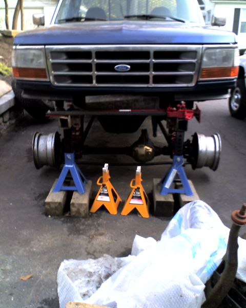 1996 Ford F-150 - The front axle of a blue Ford truck is supported by jack stands as it undergoes maintenance.