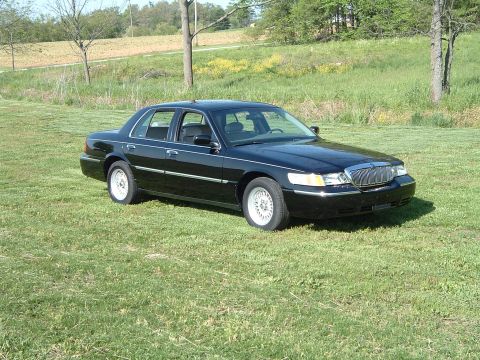 2001 Mercury Grand Marquis - A black 2001 Mercury Grand Marquis sedan is parked on a grassy field with trees in the background.