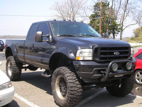 1995 Ford Bronco - A lifted Ford F-250 pickup truck with aggressive tires is parked in a lot next to other vehicles.