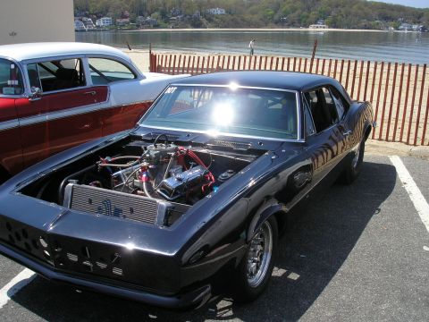 1995 Ford Bronco - A modified 1967 Chevrolet Camaro with its hood open, revealing a powerful engine, parked outdoors near a body of water.