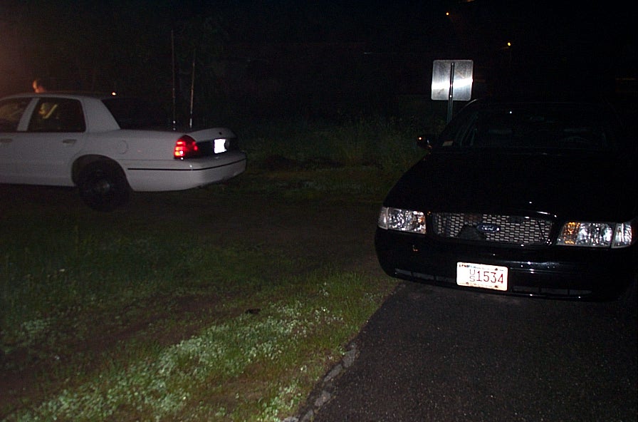 Front view of a black 2001 Ford Crown Victoria with a license plate reading 1534, parked next to a white Crown Victoria