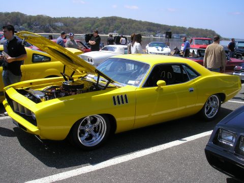 1995 Ford Bronco - A bright yellow 1970 Plymouth Barracuda is displayed with its hood open at an outdoor car show.