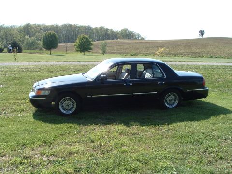 2001 Mercury Grand Marquis - A black sedan is parked on a grassy area with a rural landscape behind it.