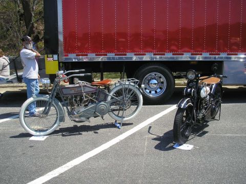 1995 Ford Bronco - Two vintage motorcycles are displayed outdoors next to a large red truck.