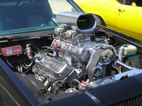 1995 Ford Bronco - A highly modified V8 engine features a prominent chrome supercharger and custom valve covers, with another vehicle visible behind it.
