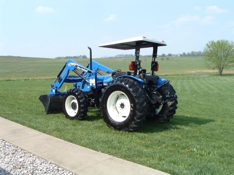 1984 Honda ATC 250 R - A blue tractor with a front loader sits on a green lawn under a clear sky.