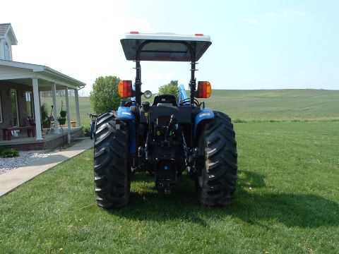 1984 Honda ATC 250 R - Rear view of a blue tractor with large tires and a canopy, situated on a grassy lawn next to a residential building.