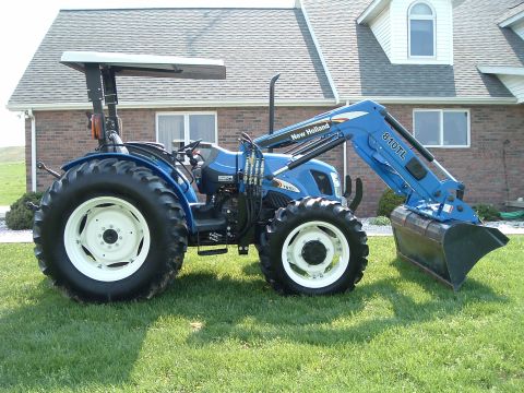 1984 Honda ATC 250 R - A blue New Holland tractor equipped with a front loader is shown from the side on a grassy lawn.