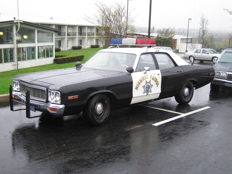 Black and white CHP Highway Patrol classic four-door sedan parked in wet lot